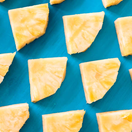 Spring or summer concept : Close up patter of many pieces of yellow pineapple laying on blue wooden table background.の写真素材