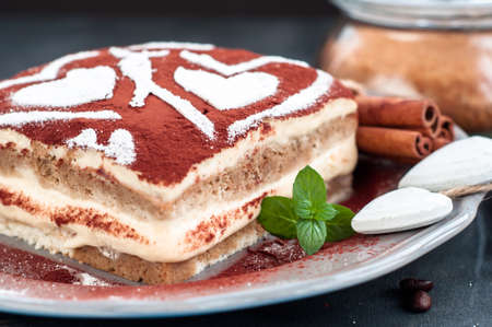Tiramisu cake on a gray plate decorated with hearts of powdered sugarの写真素材