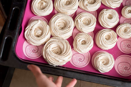 White tasty meringues baking in oven, cooking food