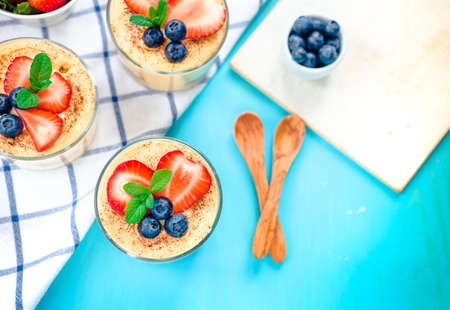 homemade, exquisite dessert tiramisu in glasses decorated with strawberry, blueberry, mint on blue...