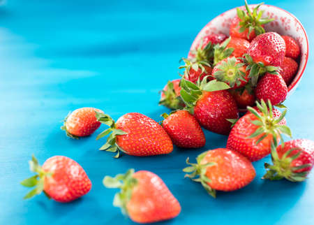 fresh bright strawberries spilled out of the bowl on blue backgroundの写真素材