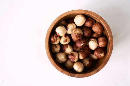 Hazelnut with peeled hazelnuts in brown bowl on textured woodenの写真素材