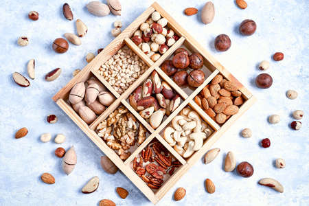 Assortment of nuts in a wooden box, on a blue background. pecans, hazelnuts, almonds, pine nuts, brazil nut, cashews, Top view, flat lay.の写真素材