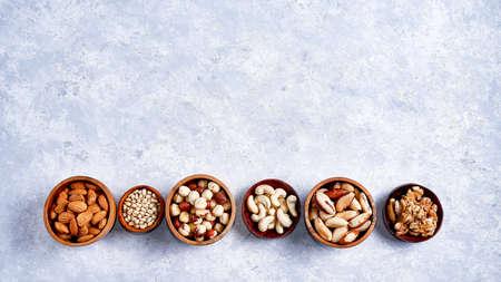 pecans, hazelnuts, almonds, pine nuts, cashews in wooden bowls on blue background, top viewの写真素材