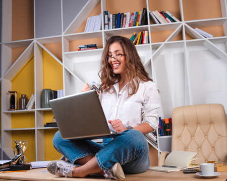 A student with glasses sits in a lotus position with a laptop