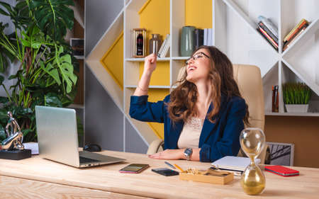Successful business woman with arms up at the table in her office