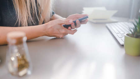 Young woman sits at a desk and types on a smartphone