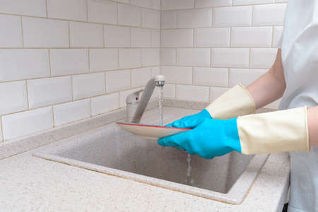 woman hand holding yellow sponge and washing saucer with washed dishes in backgroundの写真素材