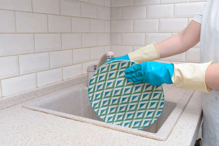 woman hand holding yellow sponge and washing saucer with washed dishes in backgroundの写真素材
