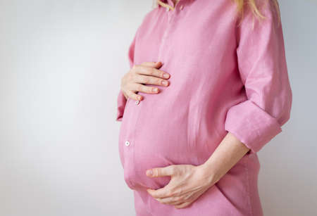 a pregnant woman stands with her hands on her stomach, the concept of expecting a babyの写真素材