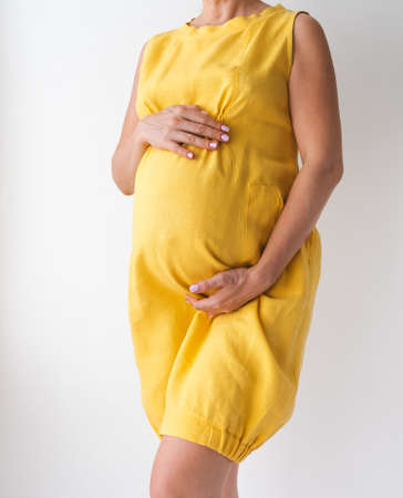 pregnant woman in a yellow dress holds her hands on her stomachの写真素材