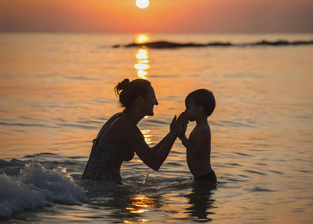 Mother and son playing in the sea at sunset. Concept of friendly family.の素材