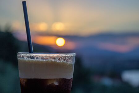 drinking ice coffee with forest and sunset on a blur background