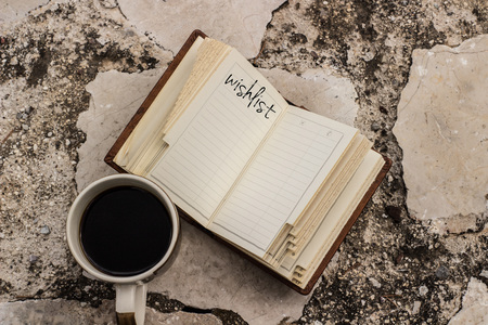 wish list notebook open book and a cup of coffee on a stone outdoor bench with copy space