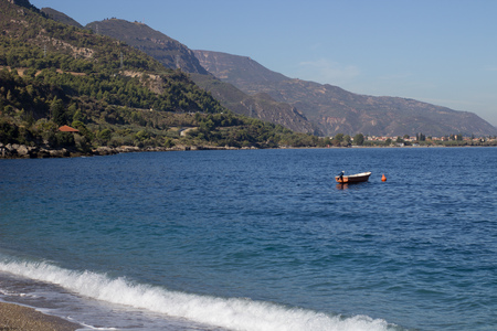 blue sea and a little boat on the water with forest on the background and small waves crashing on the beachの写真素材