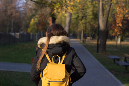 girl with backpack walking at a park with jacket and yellow bag from behind photo from behindの写真素材