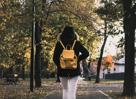 girl with backpack walking at a park with jacket and yellow bag from behind photo from behindの写真素材