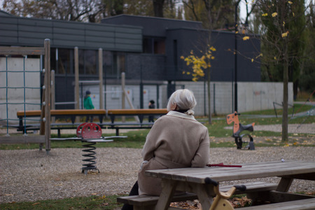 grandmother sitting on a bench watching kids play at a playground and a yellow bicycleの写真素材