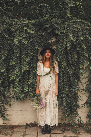 portrait of a woman standing in front of a wall full of leaves