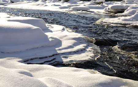 Flowing water surrounded by snowの写真素材