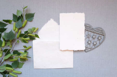 Flat lay top view mockup composition, blank card and envelope in vintage style beige paper and young birch tree branches, laced vintage heart on the light grey background, concept to display your artの写真素材