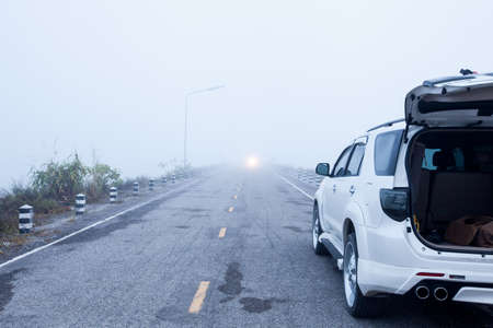 Foggy road and car stop by roadside 
