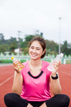 female runner smiling with hand holding energy drink and waterの写真素材