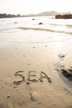Sea written in the sand at the beach waves in the background.の写真素材