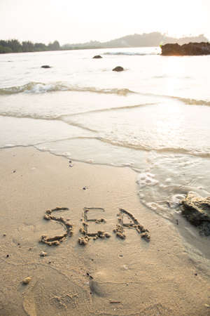 Sea written in the sand at the beach waves in the background.の写真素材