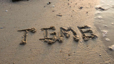 Time written in the sand at the beach waves in the background.の写真素材