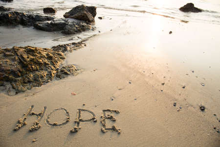 Hope written in the sand at the beach waves in the background.の写真素材