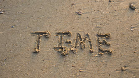 Time written in the sand at the beach waves in the background.