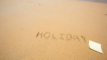 Holiday written in the sand at the beach with post it.の写真素材