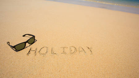 Holiday written in the sand at the beach waves in the background.の写真素材
