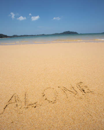 Alone written in the sand at the beach waves in the background.の写真素材