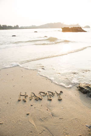Happy written in the sand at the beach waves in the background.の写真素材