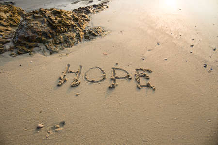 Hope written in the sand at the beach waves in the background.の写真素材