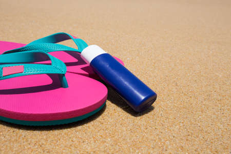 body lotion and pink flip flops on the beach.