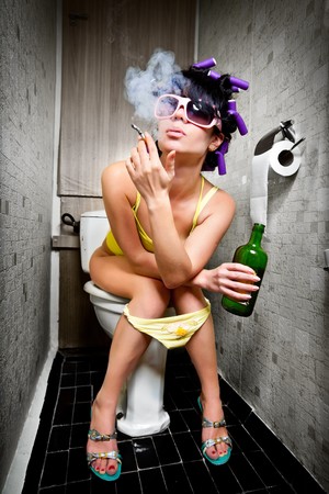 girl sits in a toilet with an alcohol bottleの写真素材