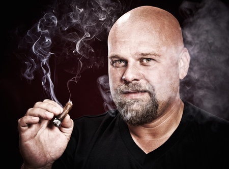 bald man with a beard smokes a cigarの写真素材