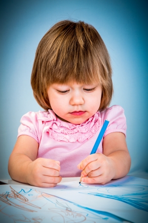 Little baby girl draws pencil on a blue backgroundの写真素材