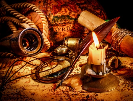 Vintage compass, magnifying glass, quill pen, spyglass lie on an old ancient map with a lit candle. Vintage still life.の写真素材