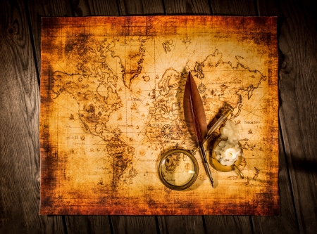 Vintage quill pen and magnifying glass lie on an old ancient map with a lit candleの写真素材
