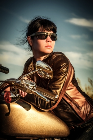 Biker girl in a leather jacket on a motorcycle looking at the sunset の写真素材