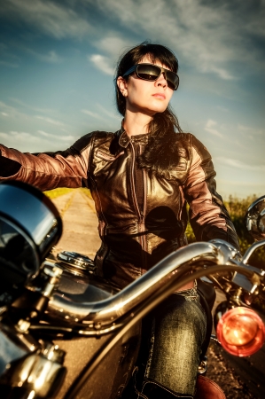 Biker girl in a leather jacket on a motorcycle looking at the sunset の写真素材