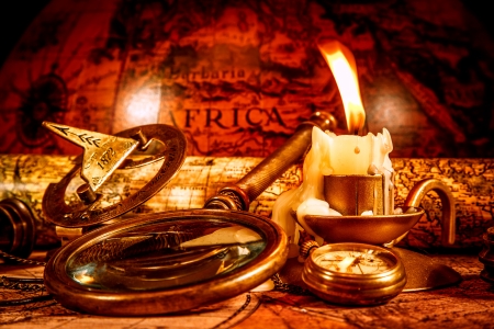 Vintage compass, magnifying glass, pocket watch, spyglass lie on an old ancient map with a lit candle  Vintage still life の写真素材