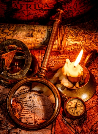 Vintage compass, magnifying glass, pocket watch, spyglass lie on an old ancient map with a lit candle  Vintage still life の写真素材