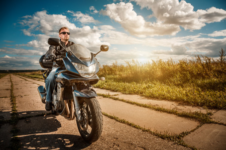 Biker man wearing a leather jacket and sunglasses sitting on his motorcycle looking at the sunset.の写真素材