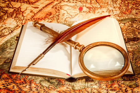 Vintage still life - magnifying glass, old book and goose quill pen lying on an old map in 1565.