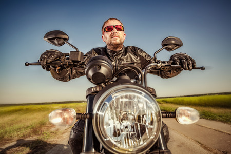 Biker in a leather jacket riding a motorcycle on the road. Filter applied in post-production.